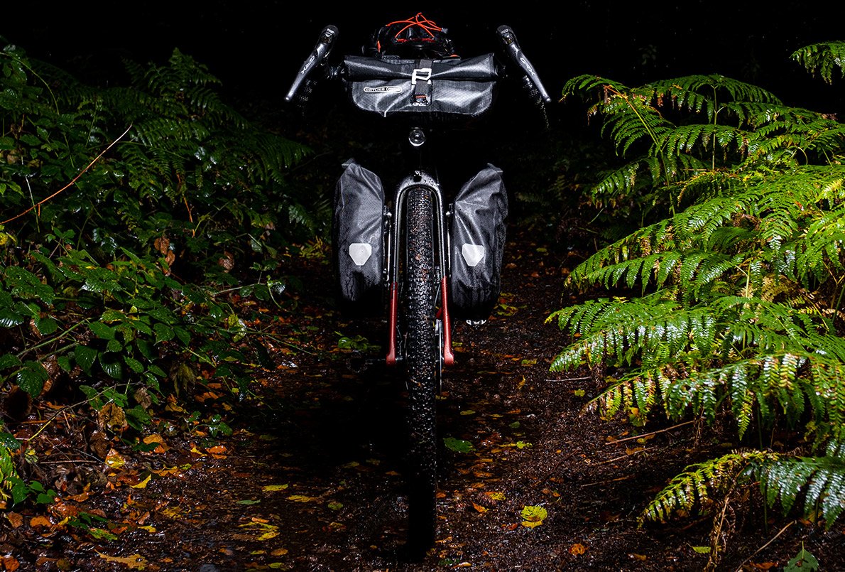 Vélo Wish One Quest Gravel noir et cuivre, de face, avec équipement bikepacking Ortlieb sur un chemin en forêt