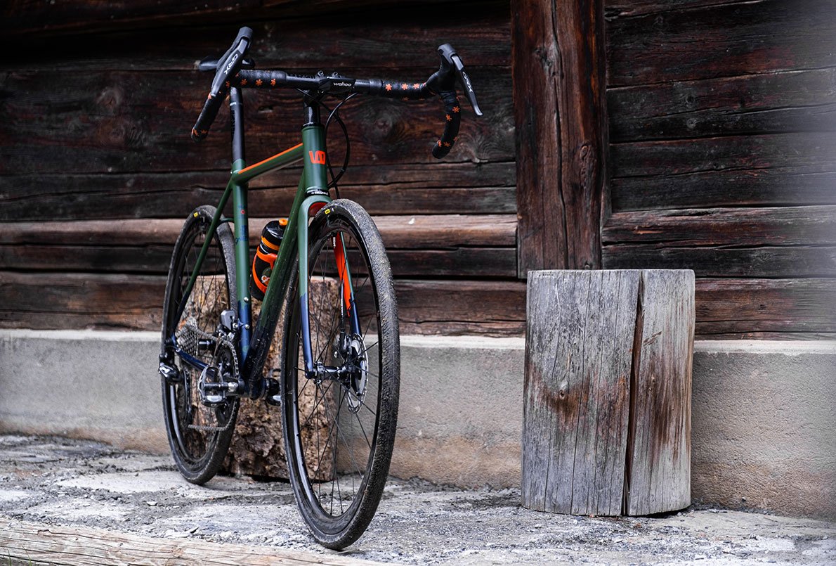 Vélo Wish One SUB Gravel vert kaki, bleu marine et orange, de face sur un fond en bois