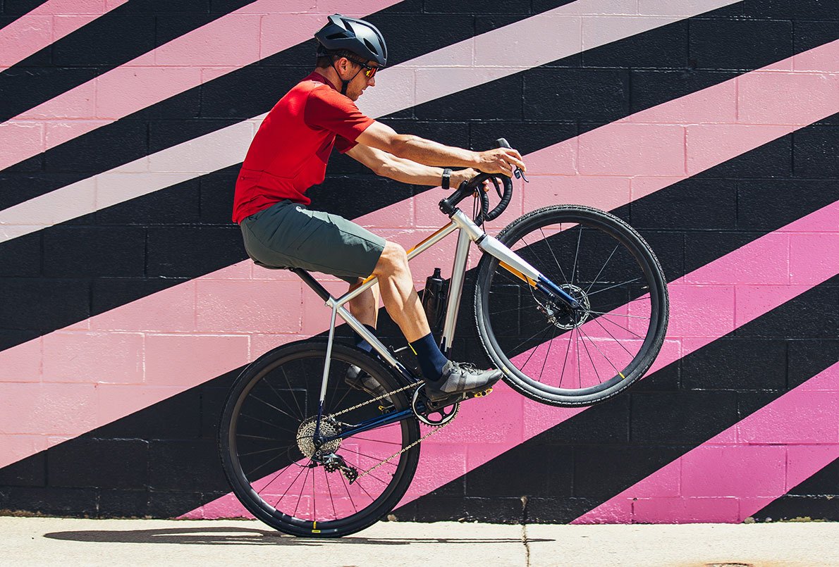 Cycliste en roue arrière sur un vélo gravel Wish One SUB sur fond coloré