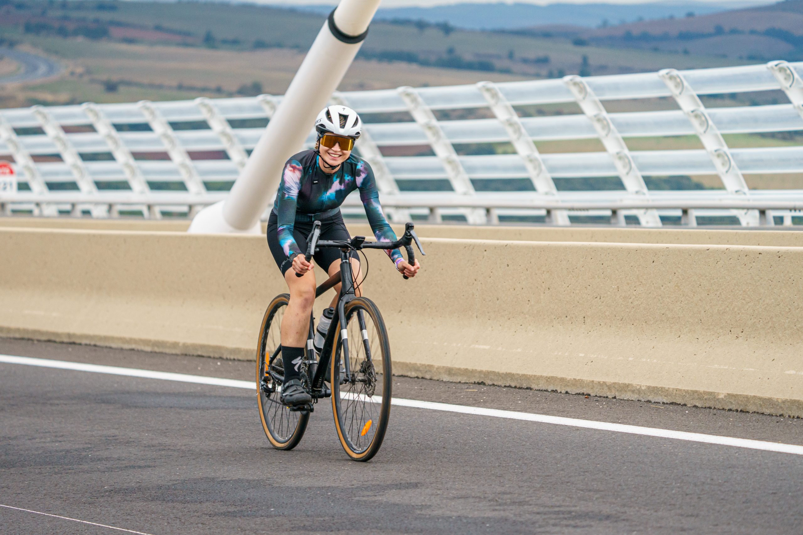 jeune femme cycliste sur son vélo gravel qui traverse le viaduc de millau